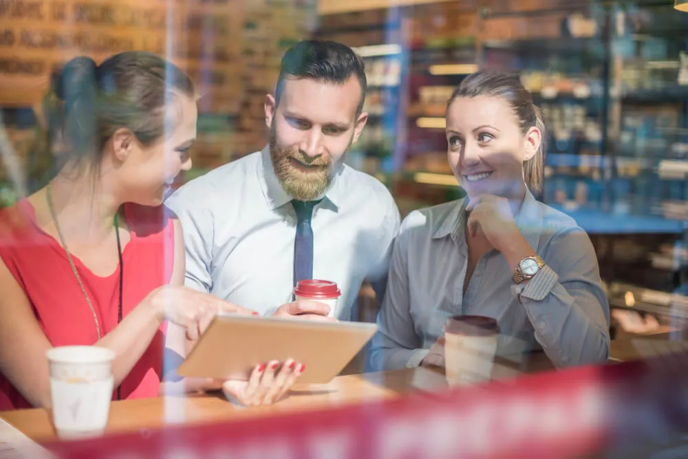 Start a business in Dubai- Three professionals having a meeting in a cafe with a tablet and coffee cups on the table. 