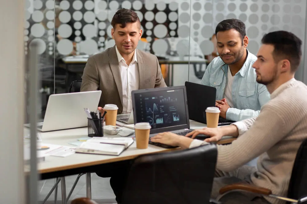 Dubai business registration - Three individuals at a meeting with laptops and coffee cups on a desk.