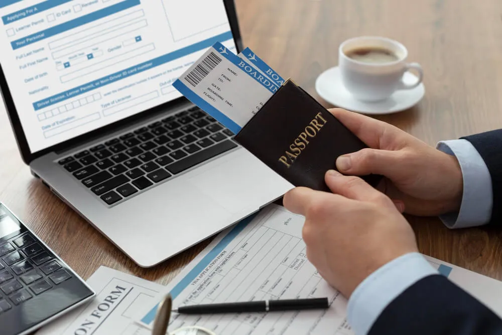 Tax-free company setup Dubai - Person holding a passport and boarding pass near a laptop displaying a flight booking site. 